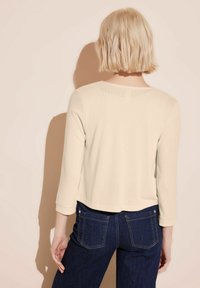 Lichtbeige cropped trui met driekwart mouwen en een subtiele textuur. Gecombineerd met donkerblauwe denim jeans, met zichtbare achterdetails.