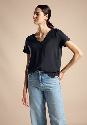 Un t-shirt noir à col en V associé à un jean bleu clair à jambes larges. Le t-shirt a des manches courtes et une coupe décontractée, avec une texture lisse.