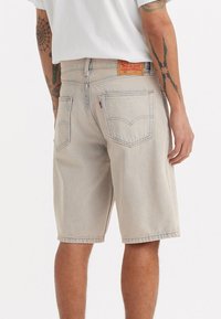 Vaaleanbeige farkkushortsit suoran leikkauksen omaavina, näkyvillä ompeleilla ja kahdella takataskulla, joissa on Levi'sin punainen lipuke oikeassa taskussa.