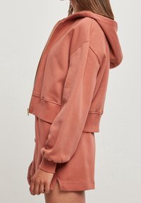 Zip-up hoodie in stoffige rozekleur, cropped ontwerp, zachte textuur, met capuchon en geribbelde manchetten. Gecombineerd met bijpassende shorts.