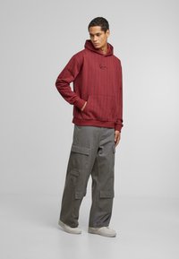 Haut à capuche rayé bordeaux avec une poche avant et un ourlet côtelé, associé à un pantalon cargo gris avec plusieurs poches et une coupe décontractée.