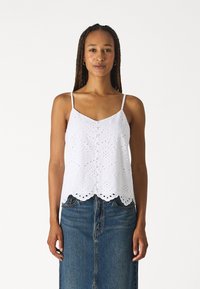 White camisole with adjustable straps, featuring eyelet embroidery, scalloped hem, and a relaxed fit, paired with a denim skirt.