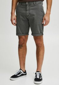 Shorts en coton gris avec des revers, dotés d'une poche avant et d'un petit logo à la taille. Associés à des baskets noires avec des lacets blancs.