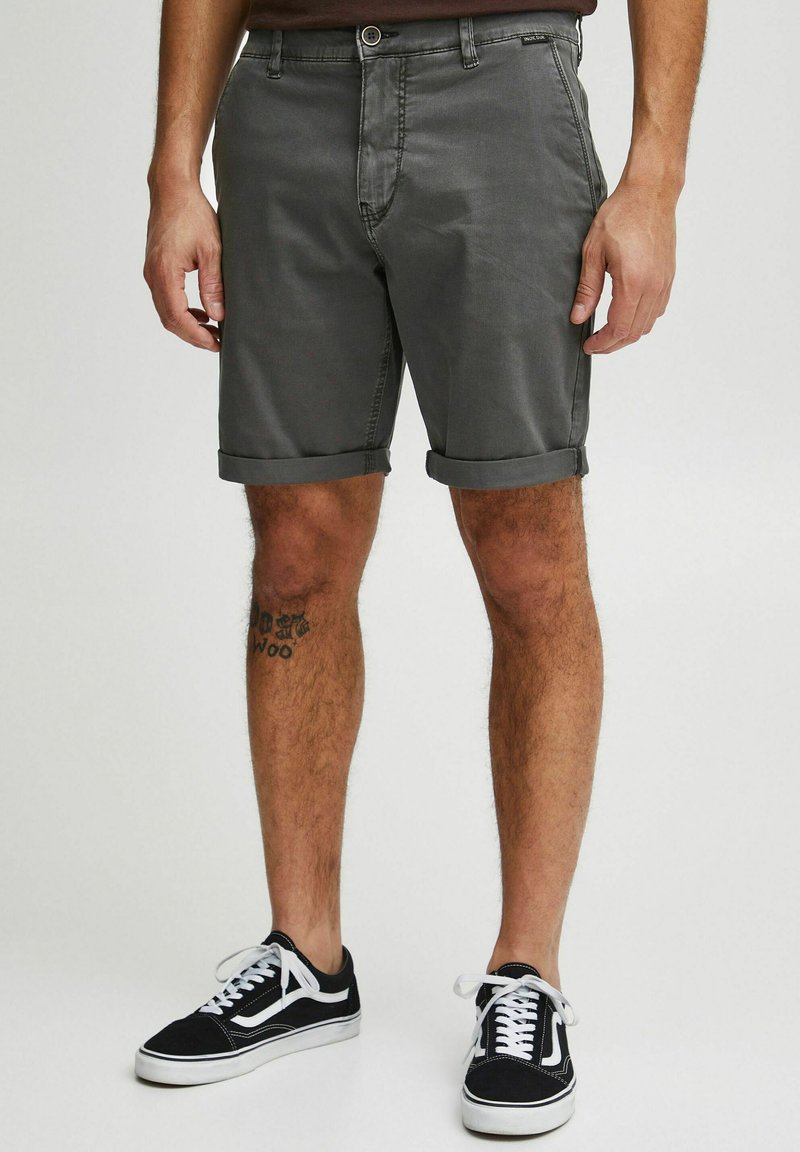 Shorts en coton gris avec des revers, dotés d'une poche avant et d'un petit logo à la taille. Associés à des baskets noires avec des lacets blancs.