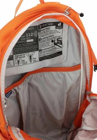 Interior de una mochila naranja con un forro gris, cremalleras e instrucciones de primeros auxilios impresas en una etiqueta. Múltiples compartimentos para una mejor organización.