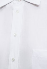 Άσπρο λινό πουκάμισο μπροστά με κουμπιά και ορατή τσέπη στο στήθος, παρουσιάζοντας την υφή του υφάσματος και τις λεπτομέρειες του γιακά.