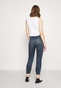 Top corto blanco con dobladillo ondulado, combinado con jeans ajustados de color azul oscuro y zapatillas altas negras.