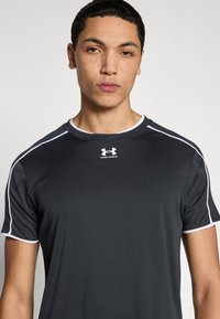 Μαύρο αθλητικό T-shirt με κοντά μανίκια, με λευκές λεπτομέρειες κατά μήκος του γιακά και των μανικιών. Κατασκευασμένο από ομαλό, υλικό που αποβάλλει την υγρασία.