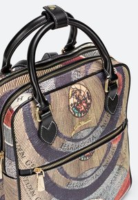 Tasche mit schwarzen Ledergriffen, detaillierter Naht, goldenen Reißverschlüssen und buntem, kreisförmigem abstraktem Muster auf texturiertem Stoff.