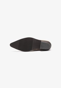 Suela de zapato con una forma puntiaguda, material de goma negra lisa, texturizada con estrías para el agarre, que presenta un leve tacón y acentos beige.