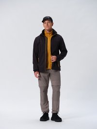Sort jakke med gule detaljer, lynlåsåbning foran. Gul lynlåsjakke under, grå cargo-bukser og sorte sneakers. Sort kasket fuldender outfittet.