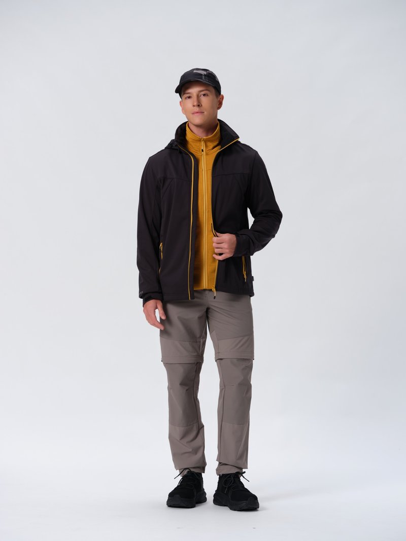 Sort jakke med gule detaljer, lynlåsåbning foran. Gul lynlåsjakke under, grå cargo-bukser og sorte sneakers. Sort kasket fuldender outfittet.