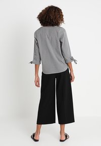 Blusa a righe grigie e bianche con maniche a tre quarti e polsini legati, abbinata a pantaloni larghi neri e infradito.