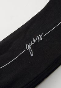 Calze nere realizzate in morbido tessuto, con il logo "guess" ricamato in bianco e dettagli con linea orizzontale. Texture liscia, senza motivi aggiuntivi.