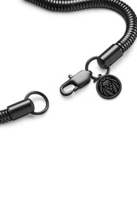 Svart metallkjed med en fleksibel, spiraldesign, med en lås og sirkulær hardware med detalj av løveemblemet.
