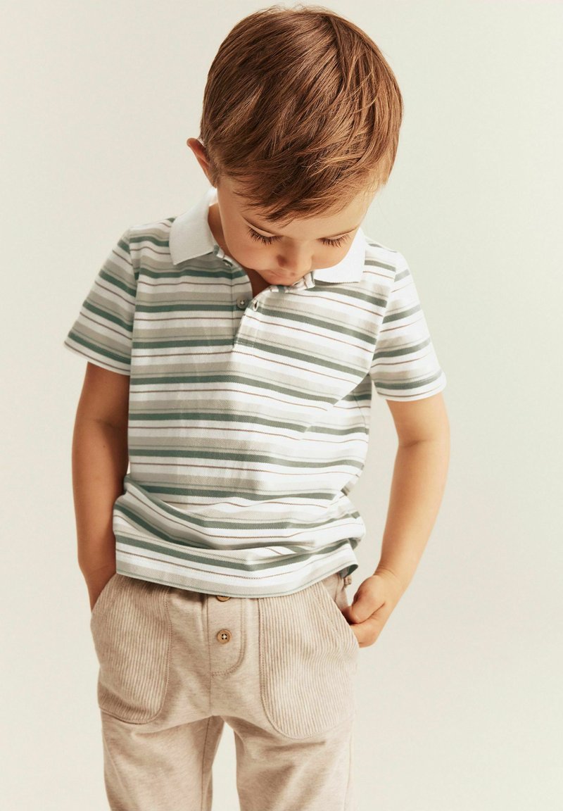 Gestreiftes Poloshirt in Weiß und Grün mit Kragen, kombiniert mit beigen Cordhosen, die über Knopfdetails und Fronttaschen verfügen.