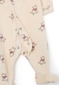 Un body de bebé color beige claro con un patrón de pequeñas ilustraciones de ositos. Tejido suave, mangas largas y cierres a presión en la parte delantera y en las piernas.