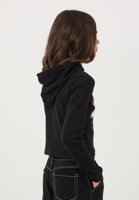 Felpa corta nera con un design testurizzato a coste e cappuccio con coulisse. Presenta stampe grafiche colorate sul davanti e una silhouette aderente.