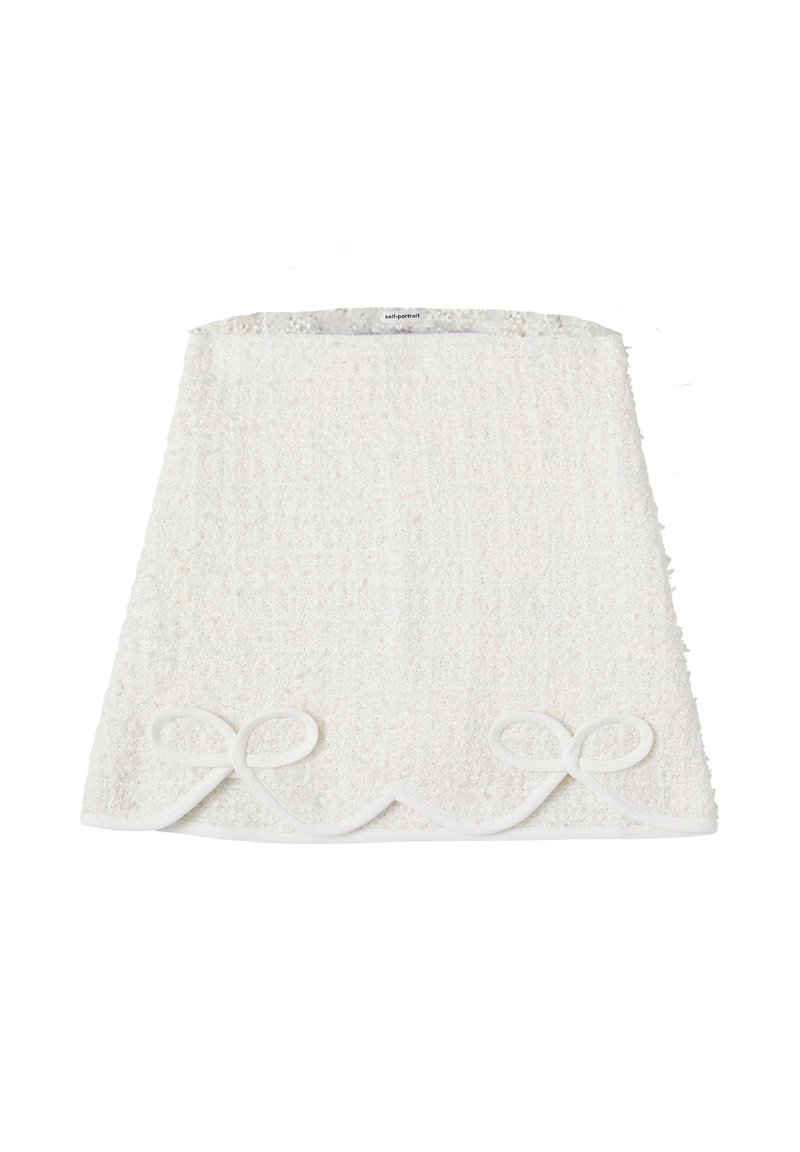 Gonna in tessuto bianco con texture, orlo a scallop e due fiocchi decorativi in fondo. Superficie morbida e soffice con una leggera lucentezza.