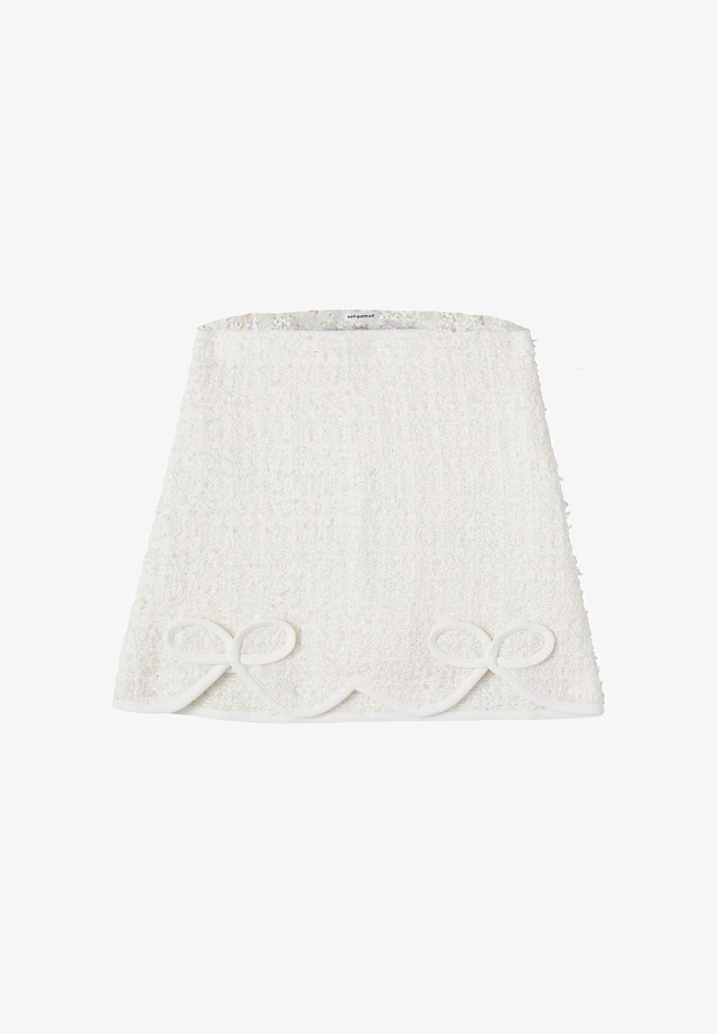 Jupe en tissu texturé blanc avec un ourlet festonné et deux nœuds décoratifs en bas. Surface douce et duveteuse avec un léger éclat.