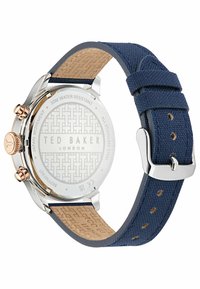 Ted Baker watch with a silver stainless steel case, navy textured strap, and a patterned leather underside. Features a rose gold crown and accents.
