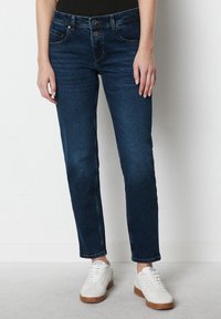 Vaqueros de denim azul oscuro con corte recto, diseño de cinco bolsillos y costuras en contraste, combinados con zapatillas blancas.