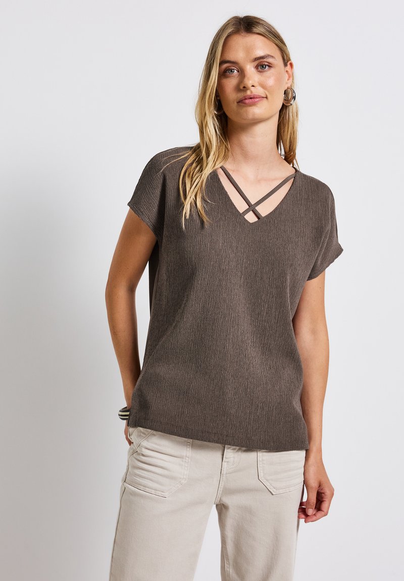 Haut court à manches courtes texturé marron avec un col en V et des bretelles croisées. Associé à un pantalon beige clair, présentant une coupe décontractée.