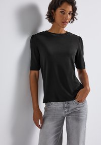 Sort kortærmet top med subtile puffærmer, lavet af glat stof. Matchet med lysegrå brede bukser. Minimalistisk design.