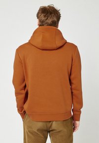 Hoodie in een warme oranje kleur, gemaakt van zachte stof. Voorzien van ribgebreide manchetten en zoom, met een relaxed fit en zonder zichtbare logo's.