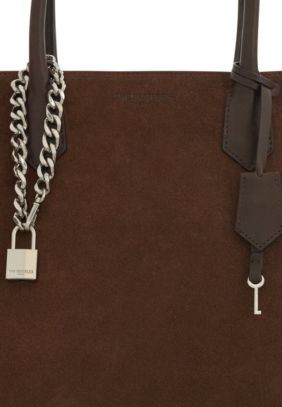 Bruine suède tote bag met leren accenten, een zilveren kettingdetail en een hangslotje met "THE KOOPLES" gegraveerd.