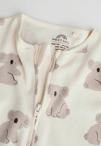 Lys crème babydragt med lynlås, prydet med et gentaget mønster af grå koala-illustrationer, fremstillet af blødt stof med en glat tekstur.