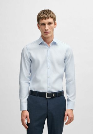 Camicia a righe blu chiaro in cotone, con maniche lunghe, colletto button-down e vestibilità slim, abbinata a pantaloni scuri e una cintura.