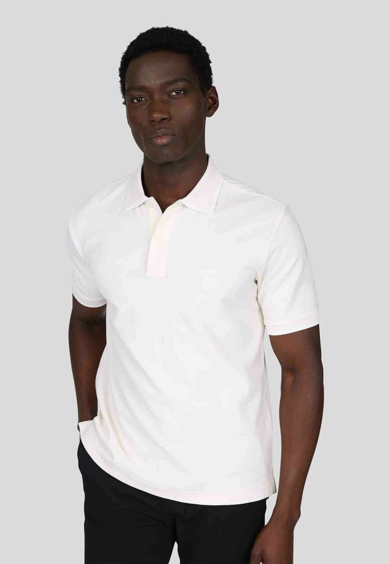 Chemise polo blanche avec un col rose clair, à manches courtes et coupe ajustée. Fabriquée en tissu lisse avec trois boutons au cou.