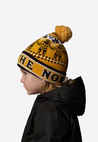 Żółta dziana czapka z pomponem, z czarno-białym wzorem i napisem "THE NORTH" na przodzie w wyraźnych czarnych literach.