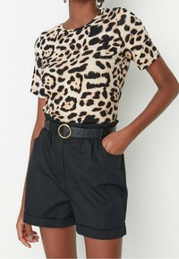Koszulka w panterkę w kolorze beżowym i czarnym, w połączeniu z czarnymi szortami z podwiniętym dołem oraz okrągłym paskiem z złotą klamrą.