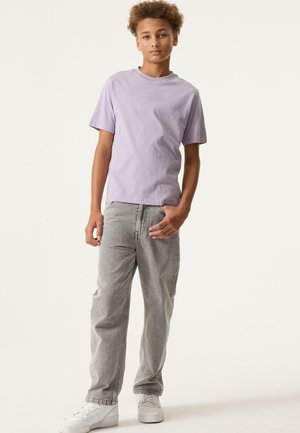 T-shirt à manches courtes couleur violet clair avec le texte "FUTURE PERSPECTIVE" ; associé à un jean gris ample et des baskets blanches. Texture de tissu lisse.