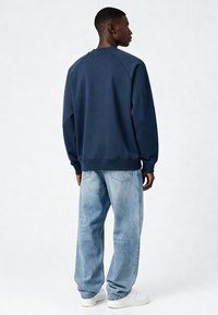 Sweat-shirt bleu marine avec manches raglan, poignets et ourlet côtelés, associé à un jean baggy bleu clair et des baskets blanches.