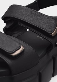 Μαύρο πλατφόρμα σανδάλι με χοντρές ρυθμιζόμενες ράβδους και κλεισίματα βέλκρο, κατασκευασμένο από υλικό συνθετικού δέρματος με υφή.