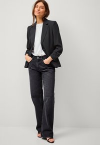 Zwarte op maat gemaakte blazer over een witte t-shirt, gecombineerd met hoogwassende flared jeans van donker denim. Sandalen met een minimalistisch ontwerp maken de outfit compleet.