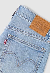 Τζιν από ανοιχτό μπλε τζιν ύφασμα με δερμάτινο έμβλημα με ανάγλυφη επωνυμία, κόκκινη ετικέτα στην τσέπη και καμπυλωτές λεπτομέρειες ραφής.