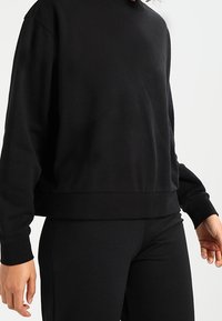 Sweat-shirt noir à col rond avec manches longues, tissu à texture douce et coupe décontractée, associé à des leggings noirs.