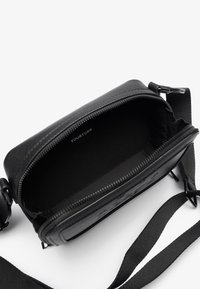 Black crossbody bag with a zip closure, smooth synthetic material, textured accents on the front, and an adjustable strap.