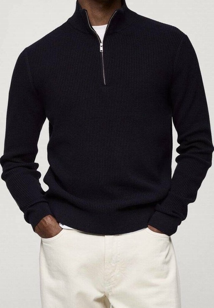 Dunkelblaues geripptes Pullover mit einem Viertel-Reißverschluss-Kragen, langärmlig und mit einem engen Saum. Getragen über cremefarbenen Hosen.