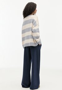 Maglione leggero a maglia con righe crema e grigio chiaro, vestibilità oversize con polsini a coste, abbinato a pantaloni larghi blu scuro.