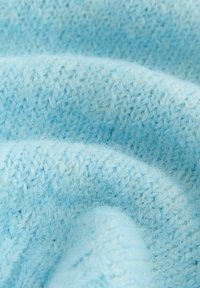 Tessuto a maglia blu chiaro con una consistenza morbida e pelosa e un motivo uniforme di punti intrecciati. Liscio e leggermente elastico.