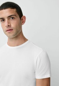 Balts T-krekls no gludas kokvilnas auduma, ar klasisku apaļu kaklu, īsām piedurknēm un pieguļošu siluetu. Minimālistisks dizains.