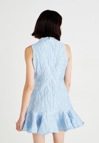 Abito senza maniche azzurro chiaro con motivo floreale testurizzato, orlo svasato e chiusura con cerniera sul retro. Nessun'altra decorazione o accento.