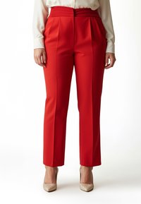 Rote, hoch taillierte Hose mit Falten, maßgeschneidertem Schnitt und glattem Stofffinish, kombiniert mit beigen, funkelnden High Heels.