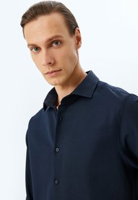 Mörk marinblå knapp-up skjorta för män med krage, subtil textur och långa ärmar. Har sex knappar och en skräddarsydd passform.