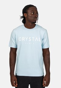 Světle modré bavlněné tričko s krátkými rukávy, kulatým výstřihem a výrazným bílým textem "CRYSTAL PARIS" přes hruď.